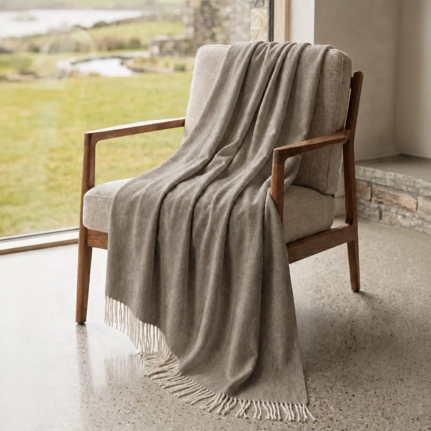 Taupe Sofadecke aus Baumwoll-Mix mit Fransen, auf einem Sessel vor einem Fenster. Ideal für Sofa & Bett.
