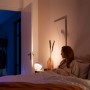 Philips Hue Iris Tischleuchte in Weiß neben einer Frau im Schlafzimmer.