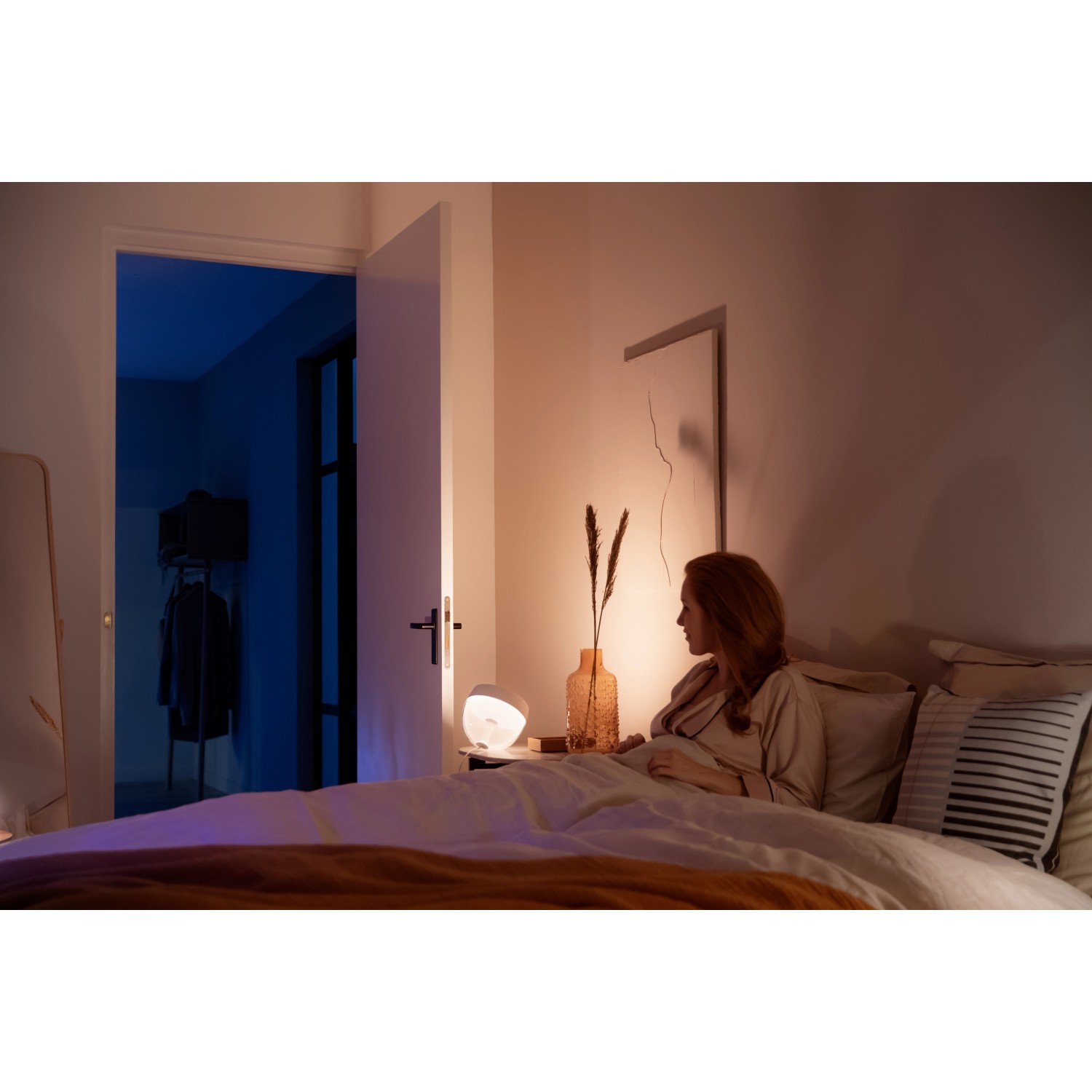 Philips Hue Iris Tischleuchte in Weiß neben einer Frau im Schlafzimmer.