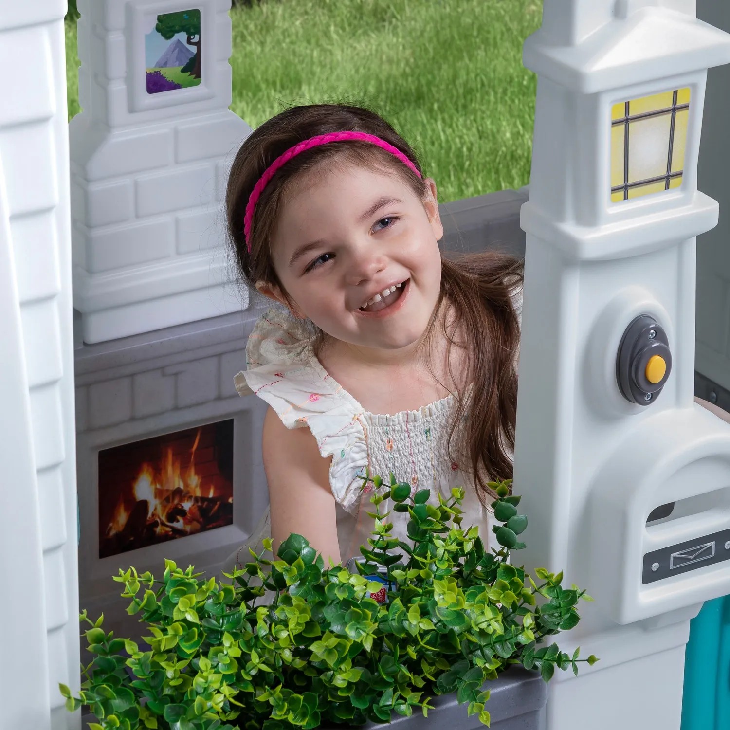 Lachendes Mädchen im Step2 Spielhaus Neat & Tidy Cottage mit Briefkasten und Kamin.