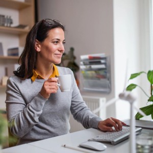 Frau am Schreibtisch, im Hintergrund transparenter Wand-Zeitschriftenhalter mit Magazinen. Praktisches Ordnungssystem für Büro & Zuhause.