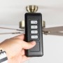 Hand hält schwarze Funk-Fernbedienung für Pepeo Deckenventilator zur Steuerung von Licht und Geschwindigkeit.