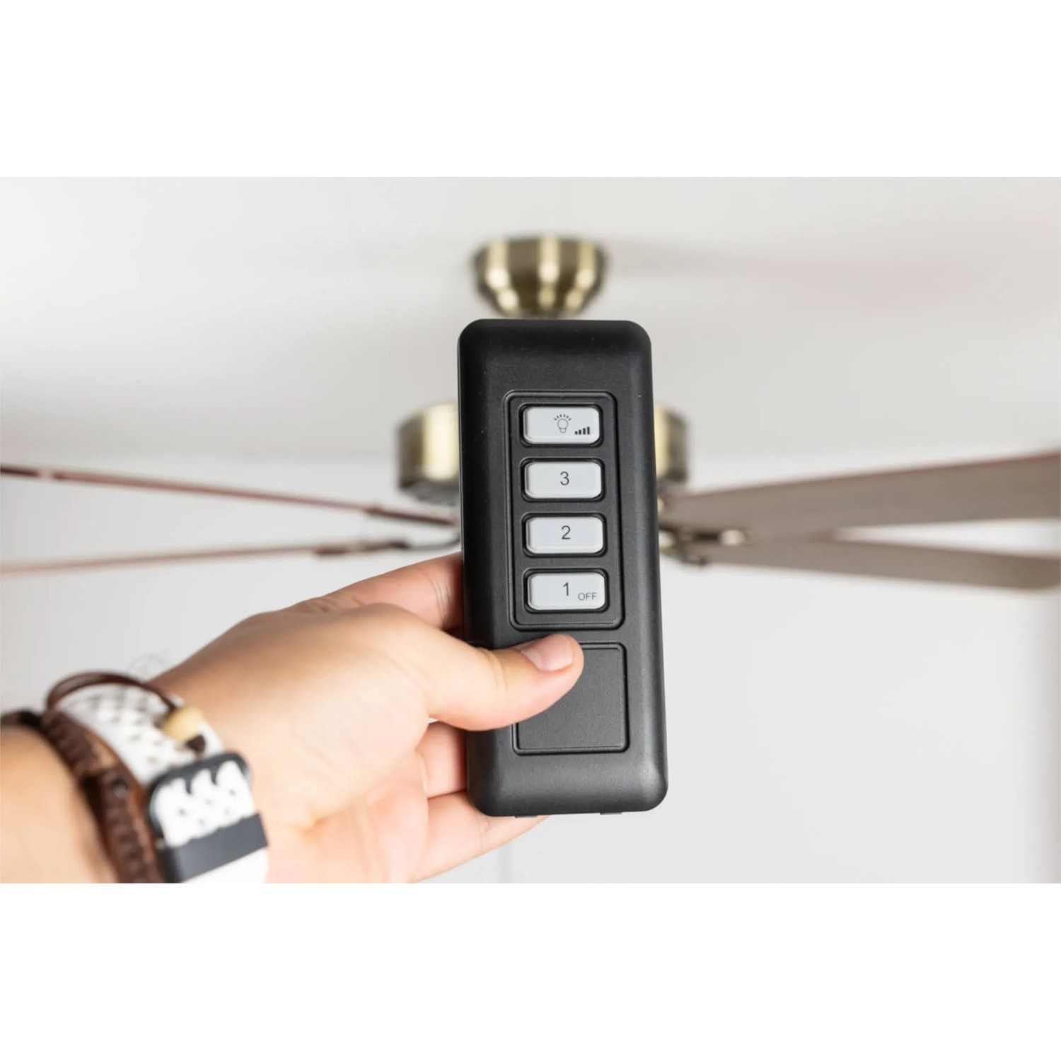 Hand hält schwarze Funk-Fernbedienung für Pepeo Deckenventilator zur Steuerung von Licht und Geschwindigkeit.