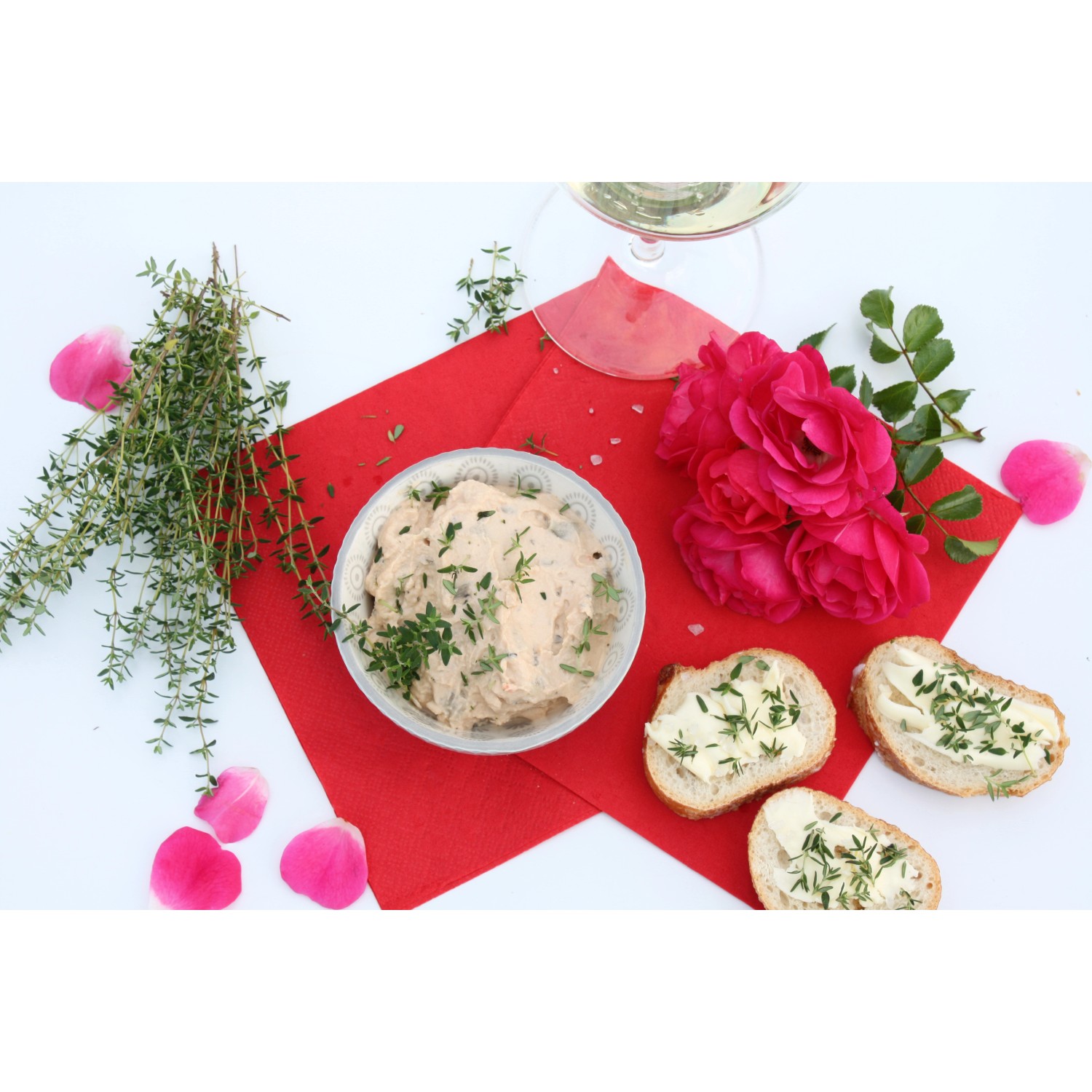 Blu Bio-Rosen-Thymian Arrangement mit Dip, Brot, Rosen und einem Glas Wein.