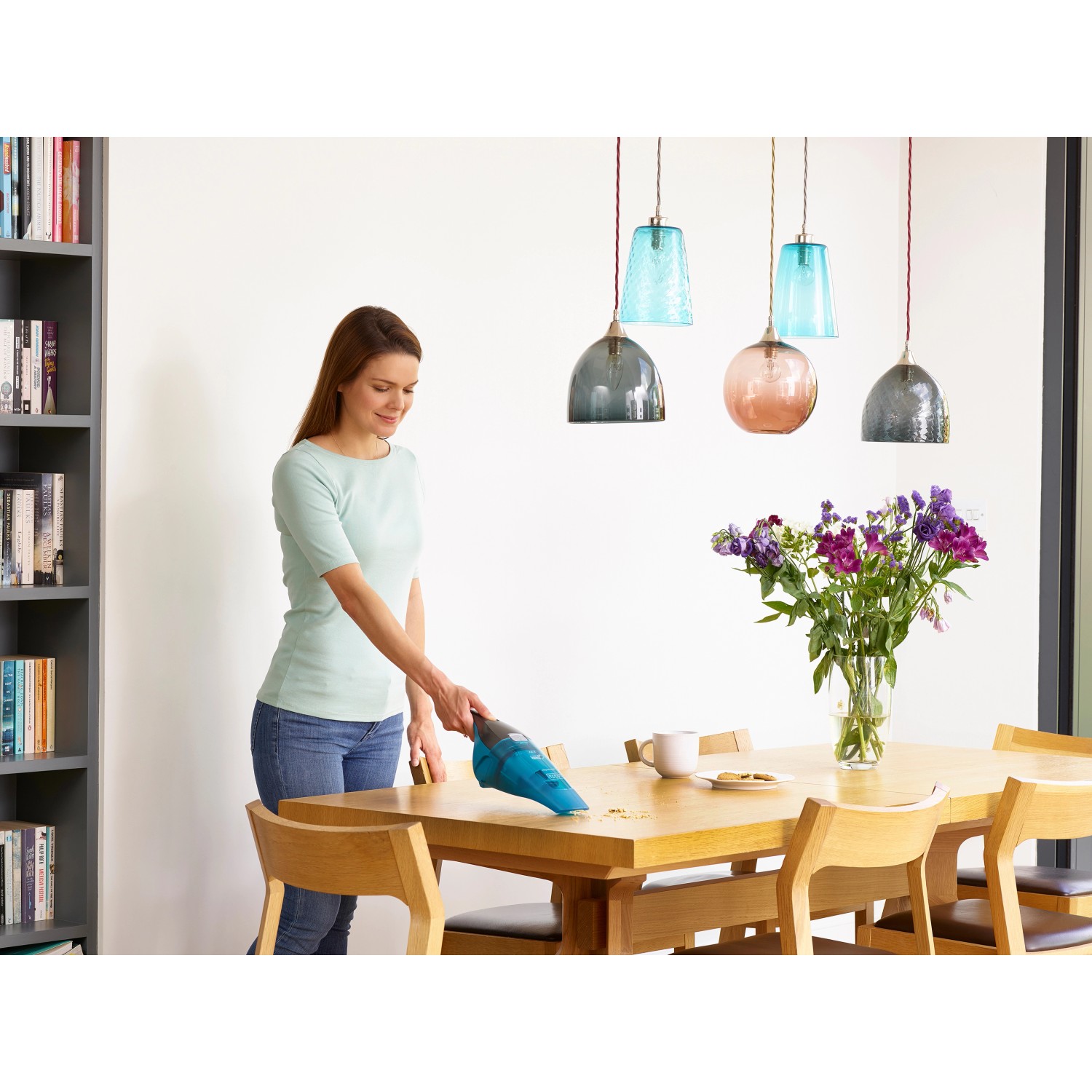 Frau saugt Krümel mit blauem Black+Decker Akku-Nass-/Trockensauger vom Holztisch.