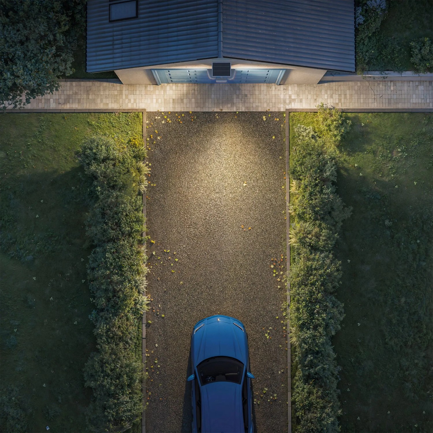 Philips Solar-LED-Außenstrahler Zyren beleuchtet Hofeinfahrt mit Auto und Haus im Hintergrund.