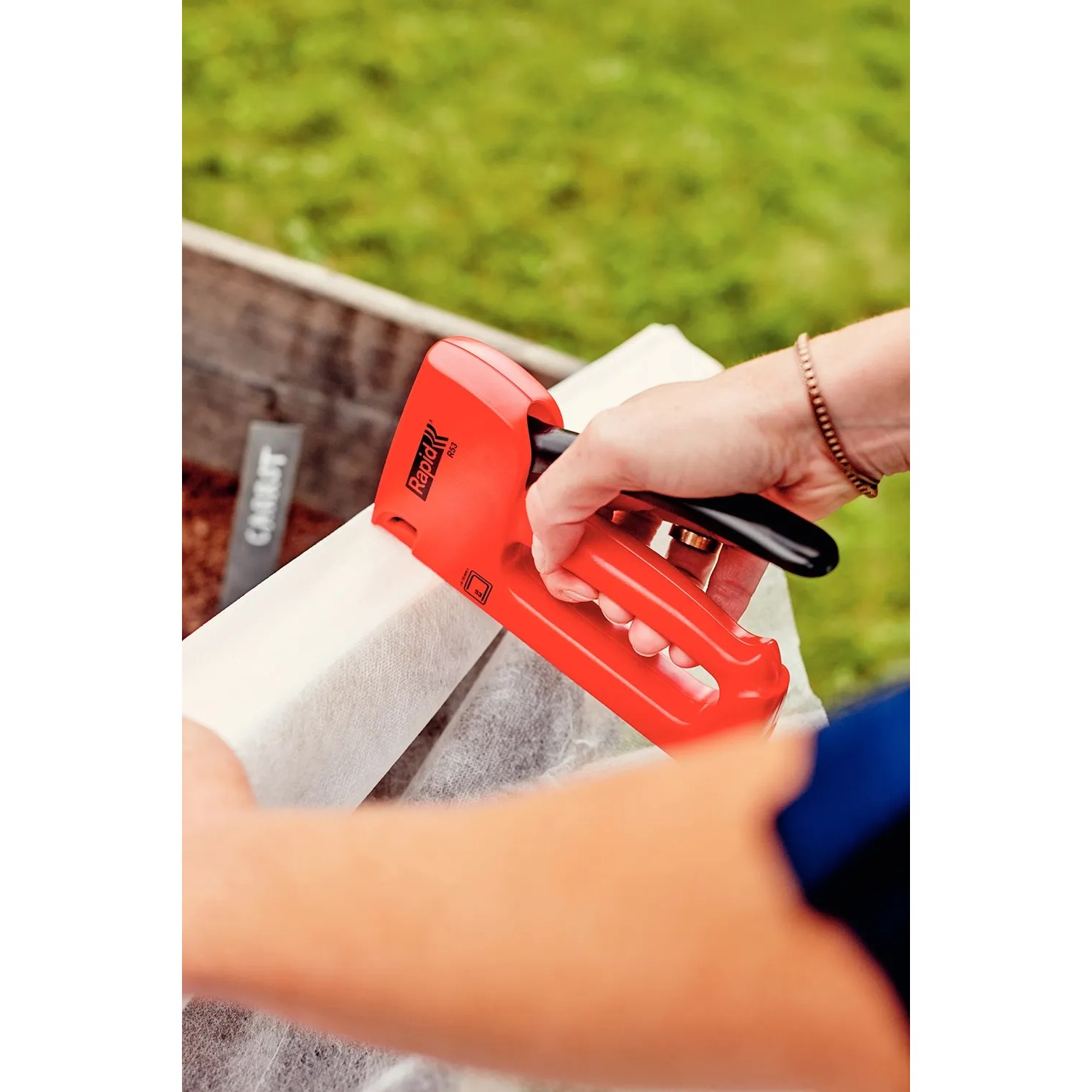 Rapid Handtacker R53 in Gebrauch: Roter Tacker befestigt Stoff an Holzrahmen im Garten.