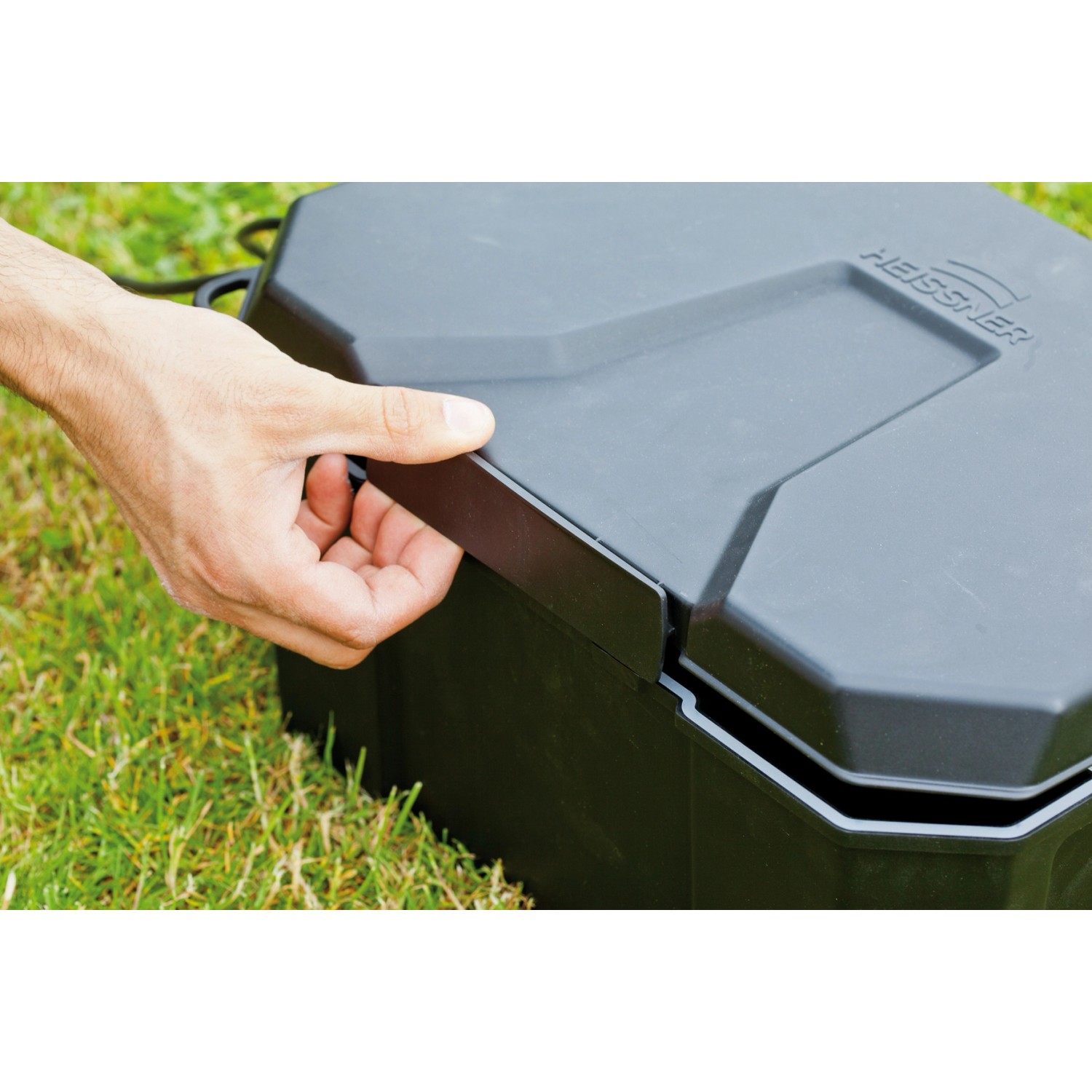 Heissner Garden Power Box, schwarze Stromverteilerbox für den Garten, wird von einer Hand geöffnet.