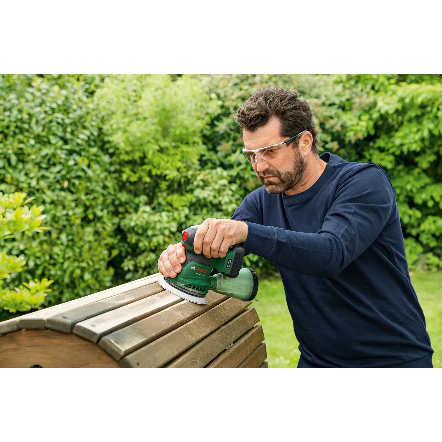 Mann schleift Holz mit dem Bosch Akku-Exzenterschleifer UniversalOrbit 18V-20. Schleifmaschine für Heimwerker.