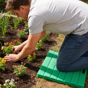 Mann kniet auf grünem, geripptem Kniekissen im Garten beim Blumen pflanzen. Gepolsterter Knieschutz.