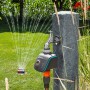 Gardena smart Water Control Bewässerungscomputer am Wasserhahn mit laufendem Rasensprenger im Garten.