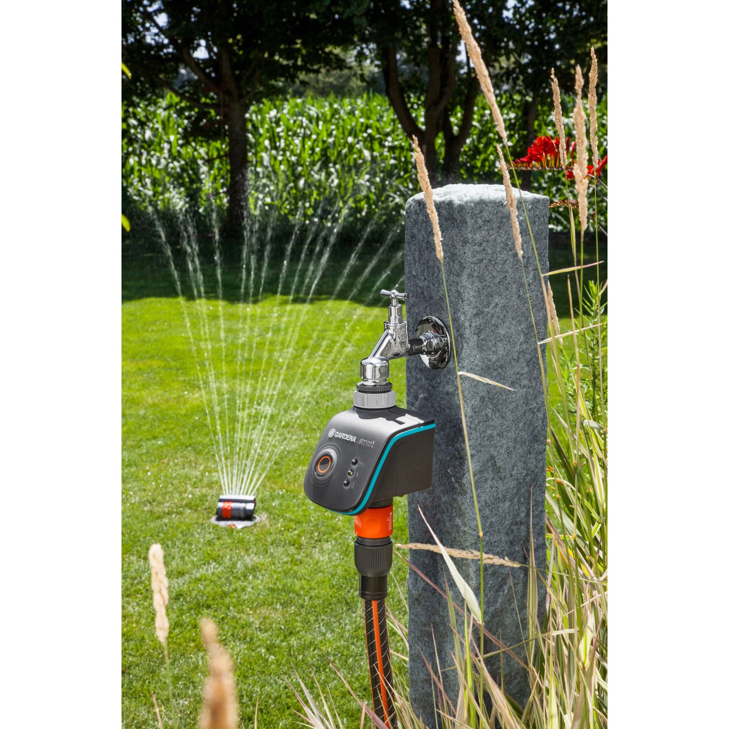 Gardena smart Water Control Bewässerungscomputer am Wasserhahn mit laufendem Rasensprenger im Garten.