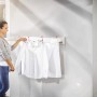 Frau hängt Wäsche auf Leifheit Wandwäschetrockner Telegant 81 Protect Plus. Ausziehbarer Wäscheständer für Wandmontage.