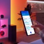 Hand steuert Philips Smart Matter Steckdose mit WiZ App auf Smartphone. Smarte Leuchten und Geräte im Raum werden bedient.