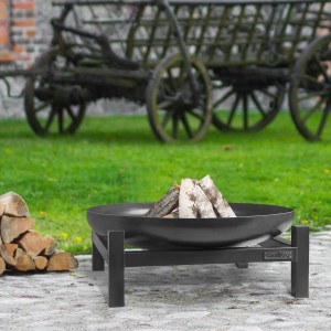 Schwarze Wilk Feuerschale Panama (Ø 60 cm) mit Holz auf einem Rasen. Im Hintergrund ein alter Wagen.