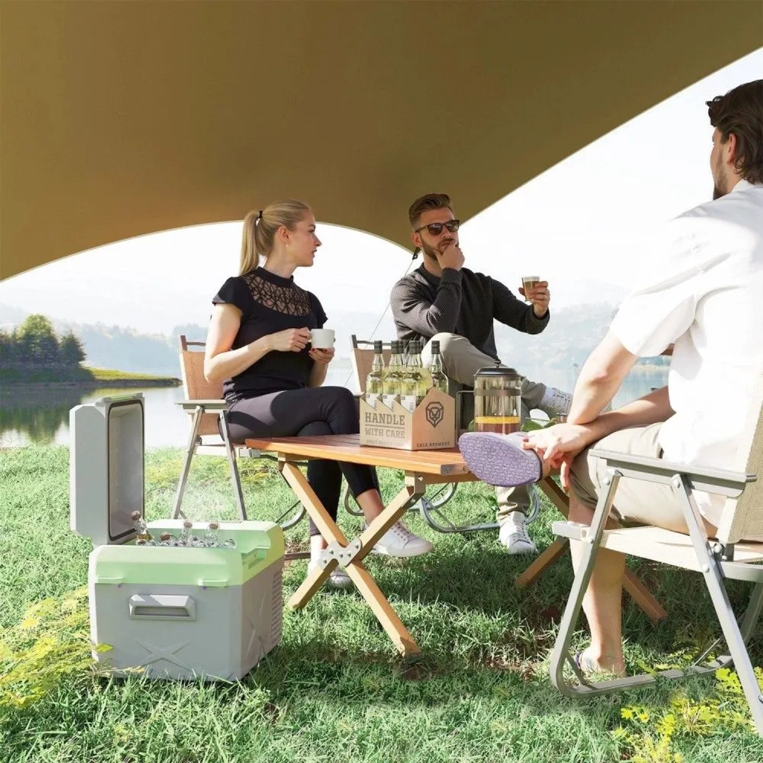 Grau-grüne Outsunny Kühlbox offen im Gras, daneben sitzen Freunde beim Camping am See. Ideal für Autozubehör & Reisen.