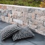 Diephaus Mauerstein Maximo Brista Muschelkalk als Gartenmauer, kombiniert mit grauen Kissen.