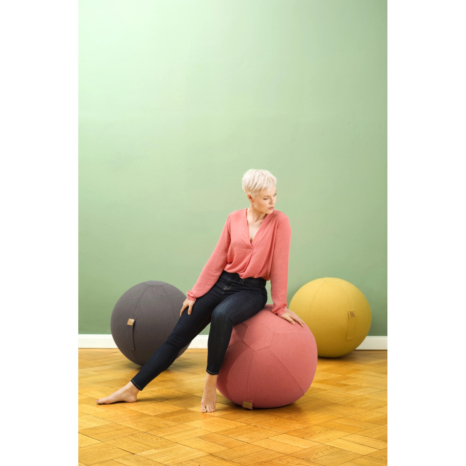 Frau sitzt auf senffarbenem Sitting Ball Hocker Felt 150l, weitere Sitzsäcke im Hintergrund.