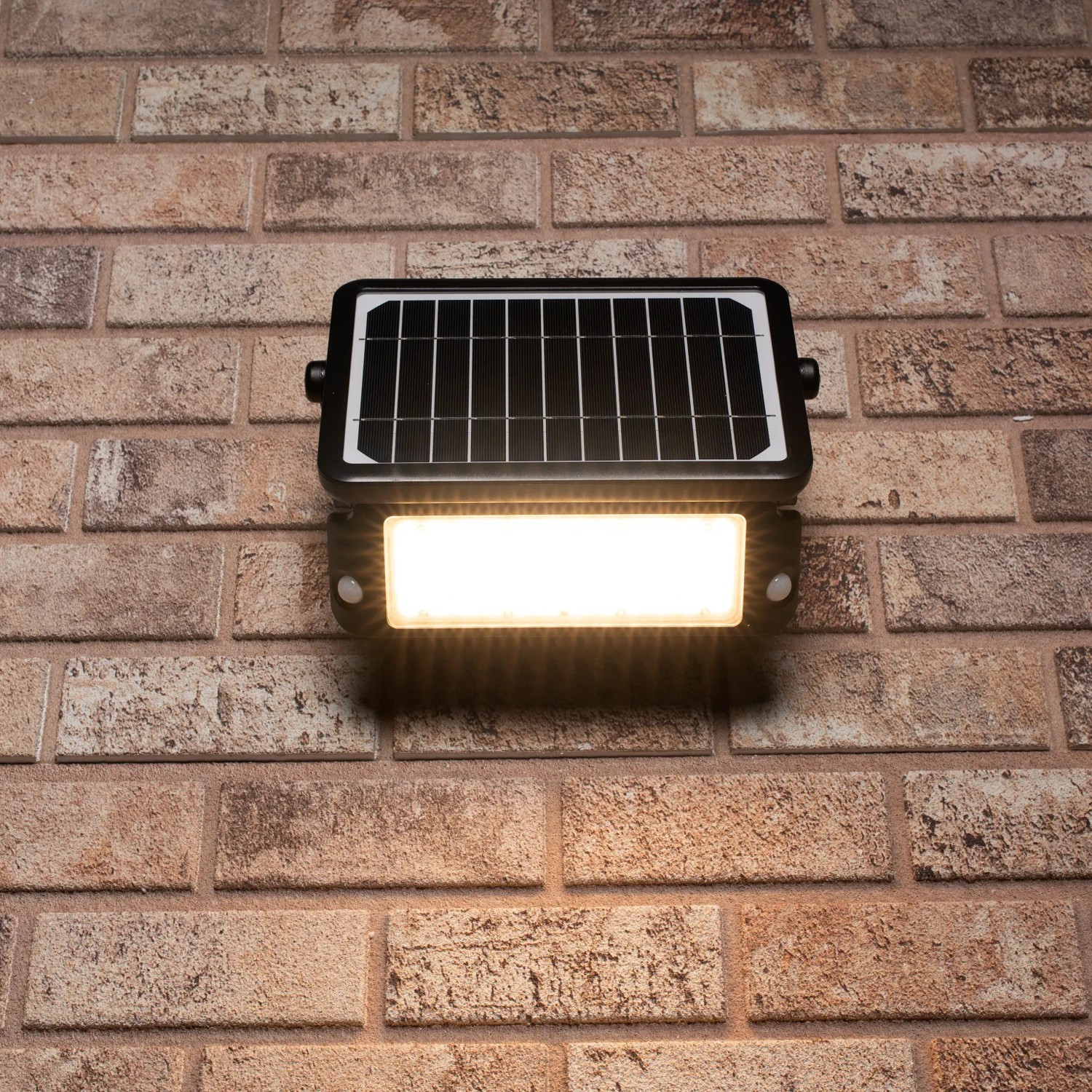 Schwarze LED Solar-Außenleuchte mit Sensor an Backsteinwand. Flutlicht mit 10W und 1.080 Lumen.