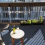 Blauer Primaflor Rasenteppich auf Balkon mit Tisch, Wein und Pflanzen.