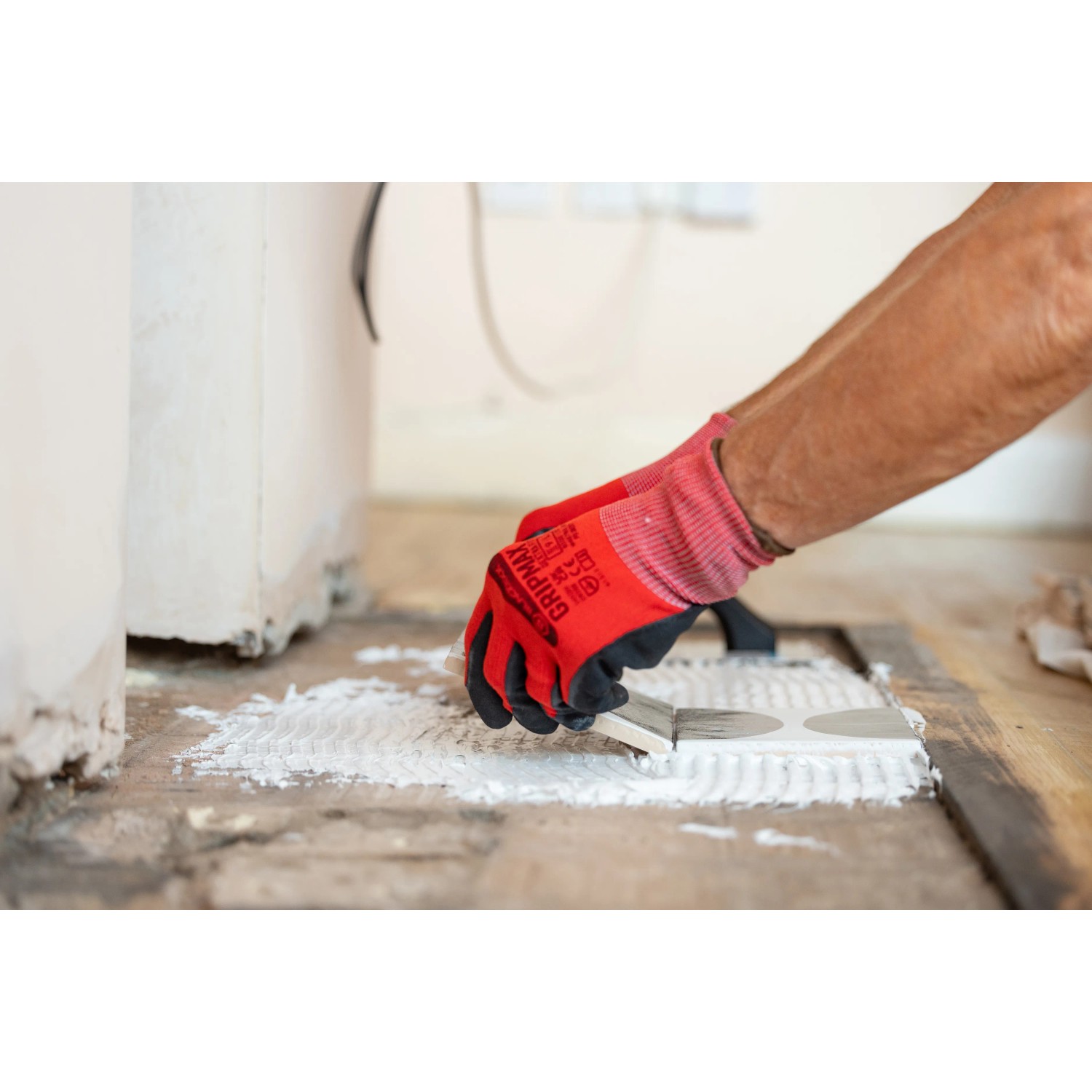 Anwendung von Soudal Fix All Floor & Wall Flächenkleber mit Spachtel, rote Handschuhe.