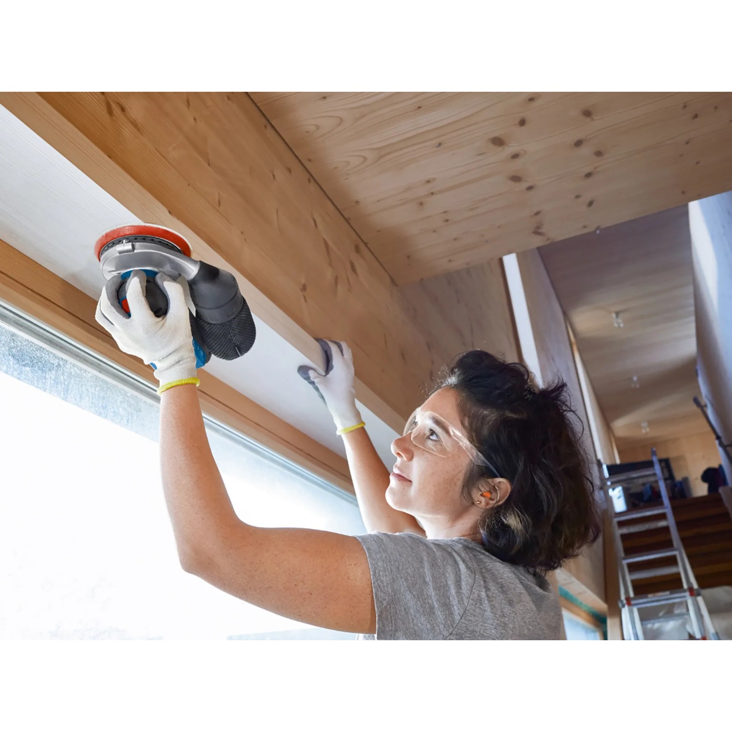 Frau schleift Holz mit Bosch Professional Akku-Exzenterschleifer GEX 18V-125. Schleifmaschine mit Schleifblatt.