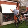 Duramax Fahrradbox in Hellbeige mit zwei Fahrrädern und zwei Personen im Garten.