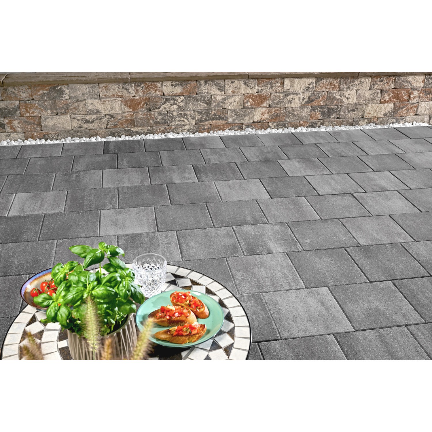 Verlegte Kann Pflastersteine Quadera in Vulkananthrazit, 30x30x6 cm, mit Tisch und Speisen im Außenbereich.