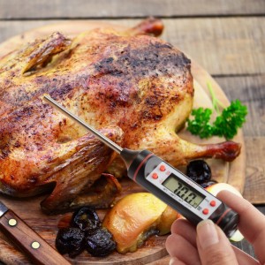 Digitales Küchenthermometer von Relaxdays misst Temperatur von Brathähnchen auf Holzbrett.