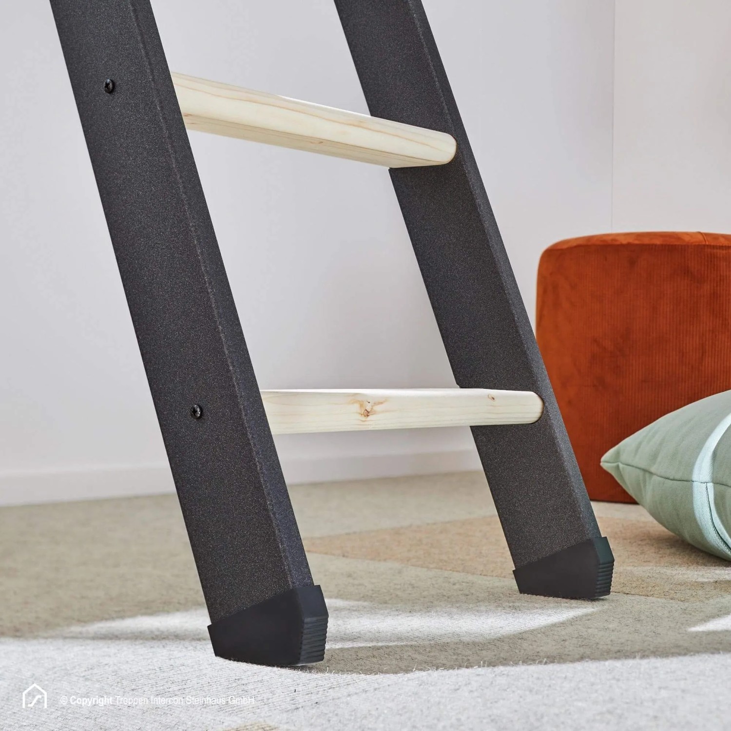 Intercon Raumspartreppe Vario mit dunkelgrauen Metallwangen und hellen Fichte-Holzstufen. Stabile Innentreppe mit schwarzen Füßen auf Teppich.