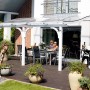 Weiße Skan Holz Terrassenüberdachung Venezia mit Polycarbonat-Dach und Familie auf der Terrasse.