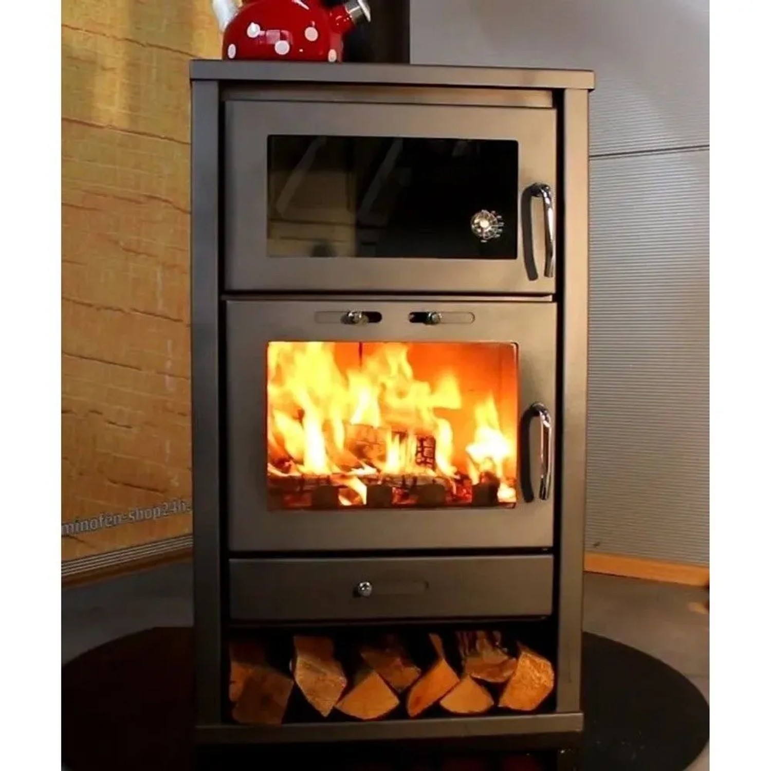Schwarzer Victoria Kaminofen Triumph F mit Backfach, brennendem Holz im Feuerraum und Holzscheiten im Fach.