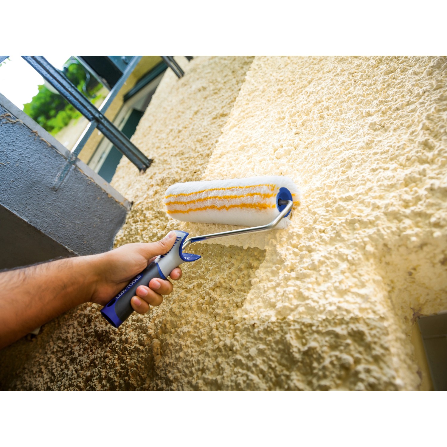LUX Dispersionswalze 25 cm im Einsatz auf grober Wandstruktur. Farbwalze mit blau-grauem Griff.