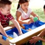 Kinder spielen am Axi Nick Sand- und Wasser-Picknicktisch mit Sonnenschirm im Garten.