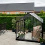 Halls Gewächshaus Popular 86, schwarzer Rahmen, 5 m², mit Pflanzen und Sitzgelegenheit im Garten.