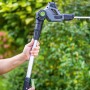 LUX-TOOLS Akku-Teleskop-Heckenschere & Astsäge mit Hand am Teleskopstiel vor Grün.