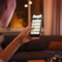 Frau steuert Philips Hue Lampe mit App auf Smartphone. White Ambiance Leuchtmittel.