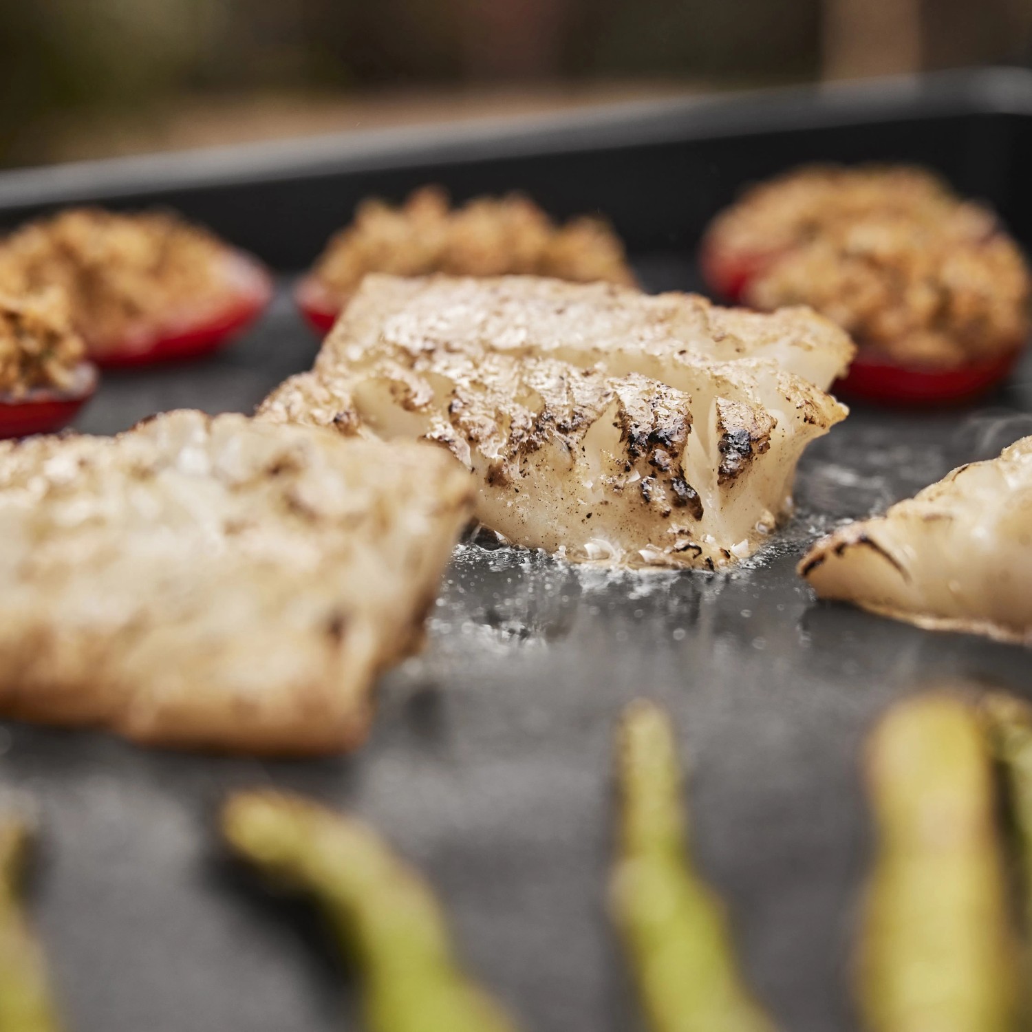 Weber Gasgrill Slate Plancha: Gegrillter Fisch, gefüllte Paprika und Spargel auf der Grillplatte.