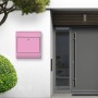 Pinker Banjado Edelstahl Briefkasten mit Rosen Motiv und Zeitungsfach an einer weißen Hauswand.