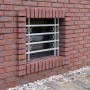 Graues, ausziehbares Stahl-Fenstergitter mit Zierelementen als Einbruchschutz an Ziegelwand. Für Kellerfenster.