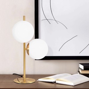 Moderne goldene Tischlampe mit zwei weißen Glaskugeln auf Holzschreibtisch. Ideal als Nachttischlampe.