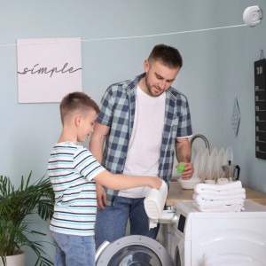 Weiße ausziehbare Kunststoff-Wäscheleine, 12m, an der Wand montiert. Vater und Sohn beim Wäschewaschen.