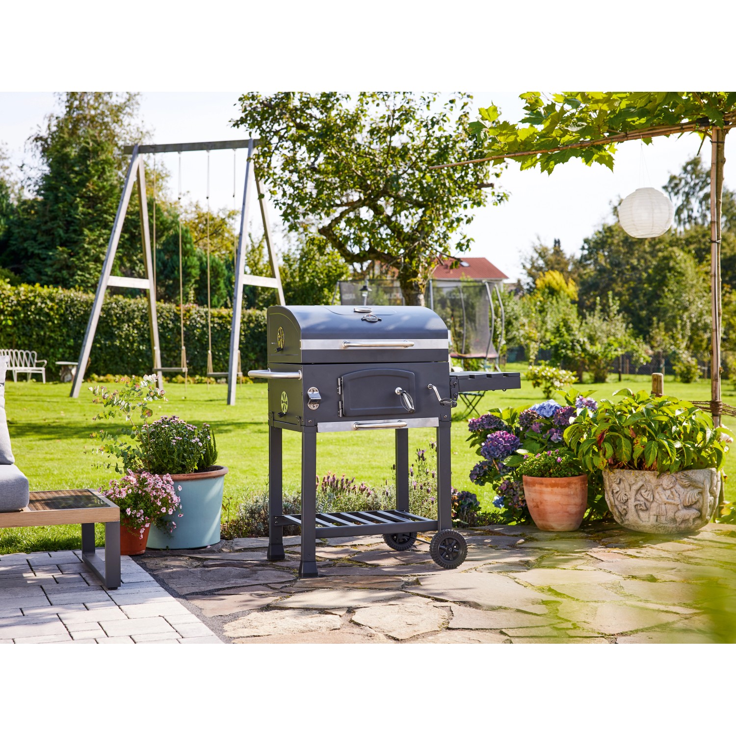 Jamestown Holzkohlegrillwagen Jaxon im Garten mit Seitentisch und Ablage.