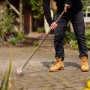 Mann reinigt mit Drahtbesen aus Buchenholz und Stahl Pflastersteine von Unkraut.