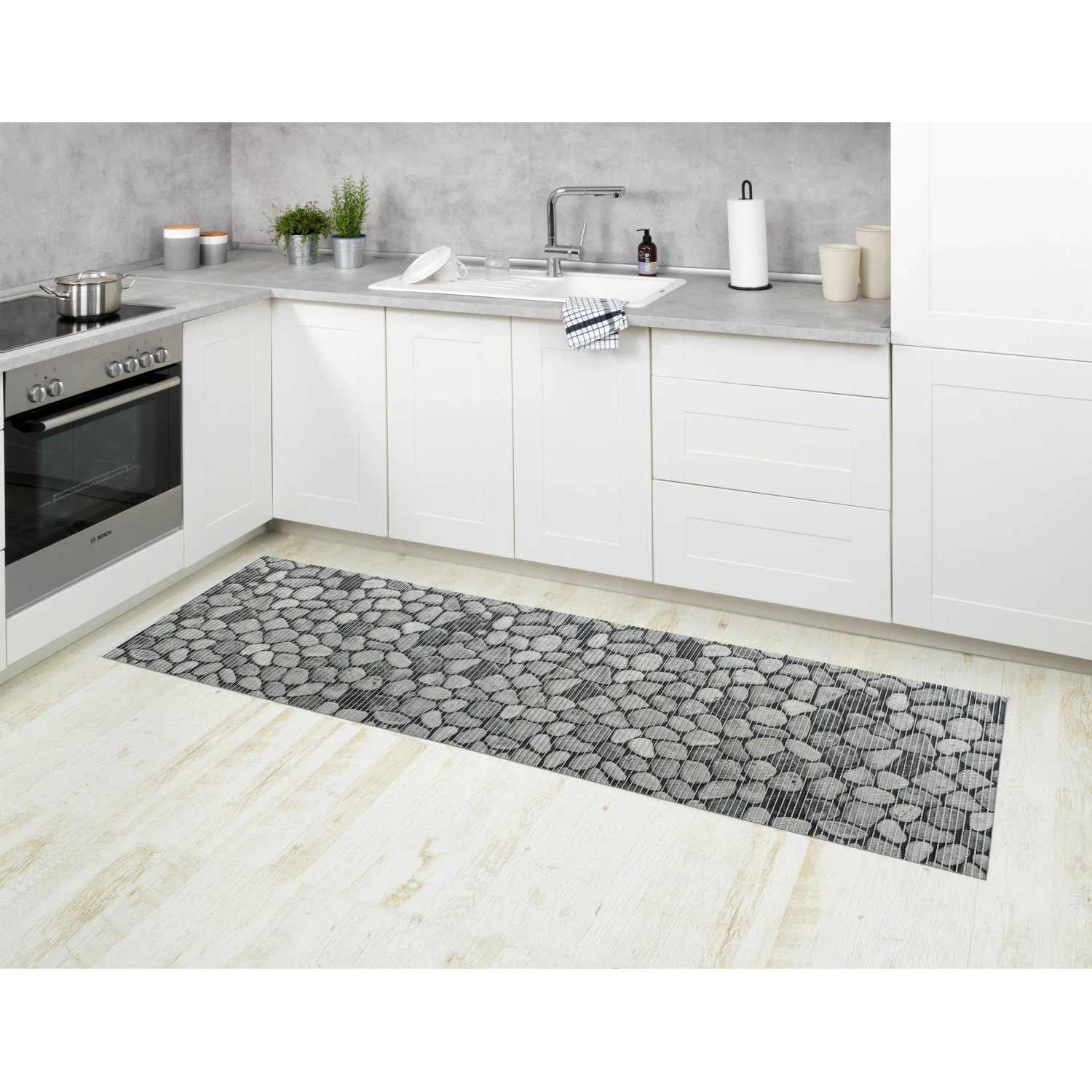 Mehrfarbige Wenko Badematte Sassi (65x200 cm) im Stein-Design als Küchenläufer vor weißer Küchenzeile.