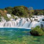 Komar Fototapete Krka Falls: Wasserfall-Szene mit blauem Himmel und grüner Natur.