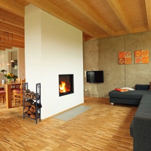 Anthrazitfarbenes Kaminholzregal aus Stahl mit 2 Ablagen, gefüllt mit Holzscheiten, neben einem Kamin. Inkl. Haken für Kaminbesteck.