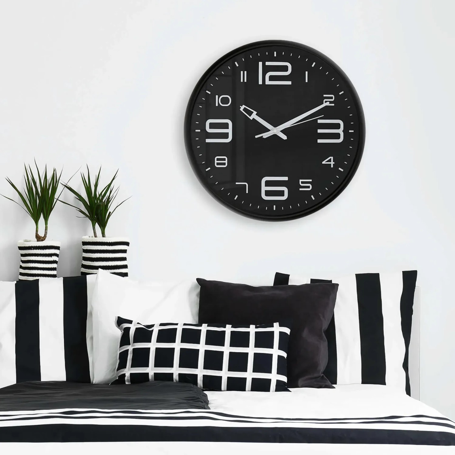 Moderne schwarze Wanduhr (Ø 38,5 cm) von Wall-Art über einem Bett mit schwarz-weißem Muster.