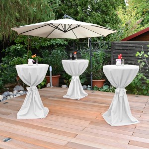 Drei weiße Beautissu Stehtischhussen Giulia Ø 70 cm im Garten unter einem Sonnenschirm.