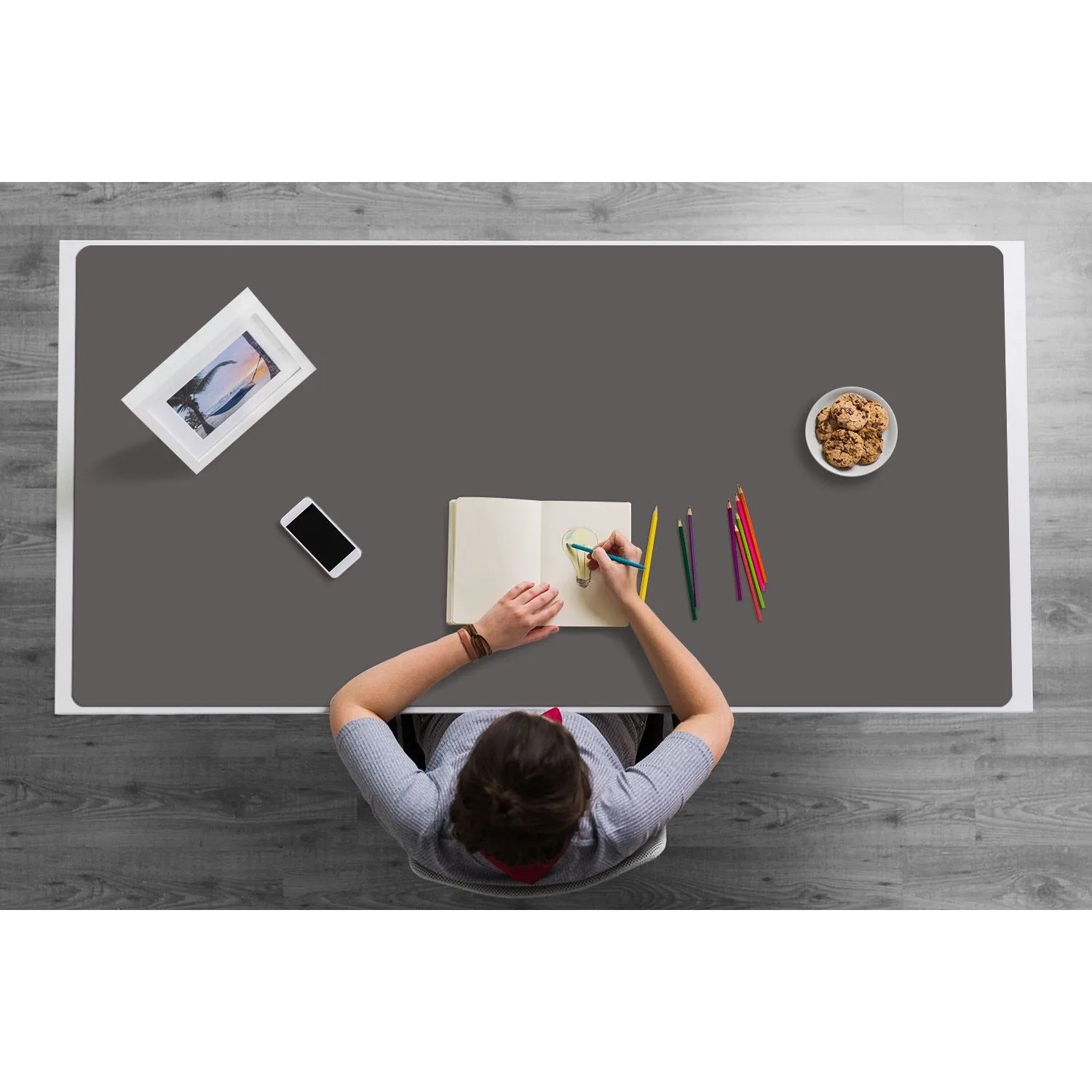 Dunkelgraue Tulup Schreibtischunterlage 100x50 cm auf weißem Tisch, Person zeichnet. Ideal als Schutzmatte für den Arbeitsplatz.